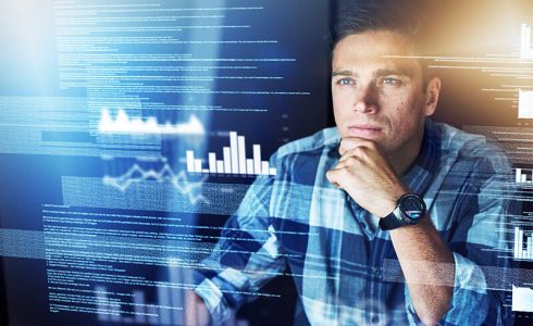 Man in blue plaid shirt looks thoughtful at text and graphs on a a digital display screen.